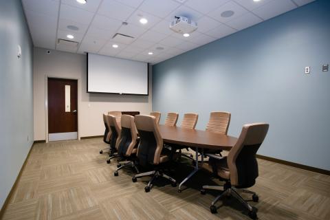 Light blue board room with conference table, chairs, and overhead projector