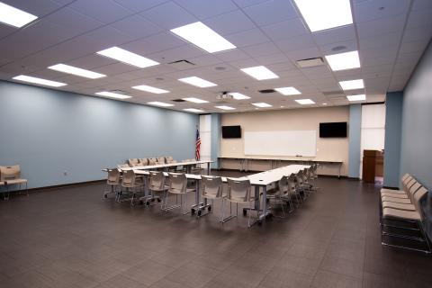 Large room with tables, chairs, two TVs, and overhead projector