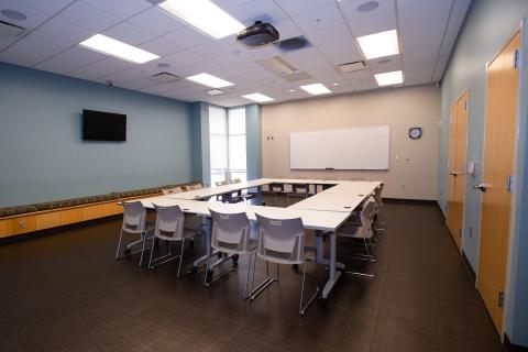 Large room with table, chairs, one TV, and overhead projector